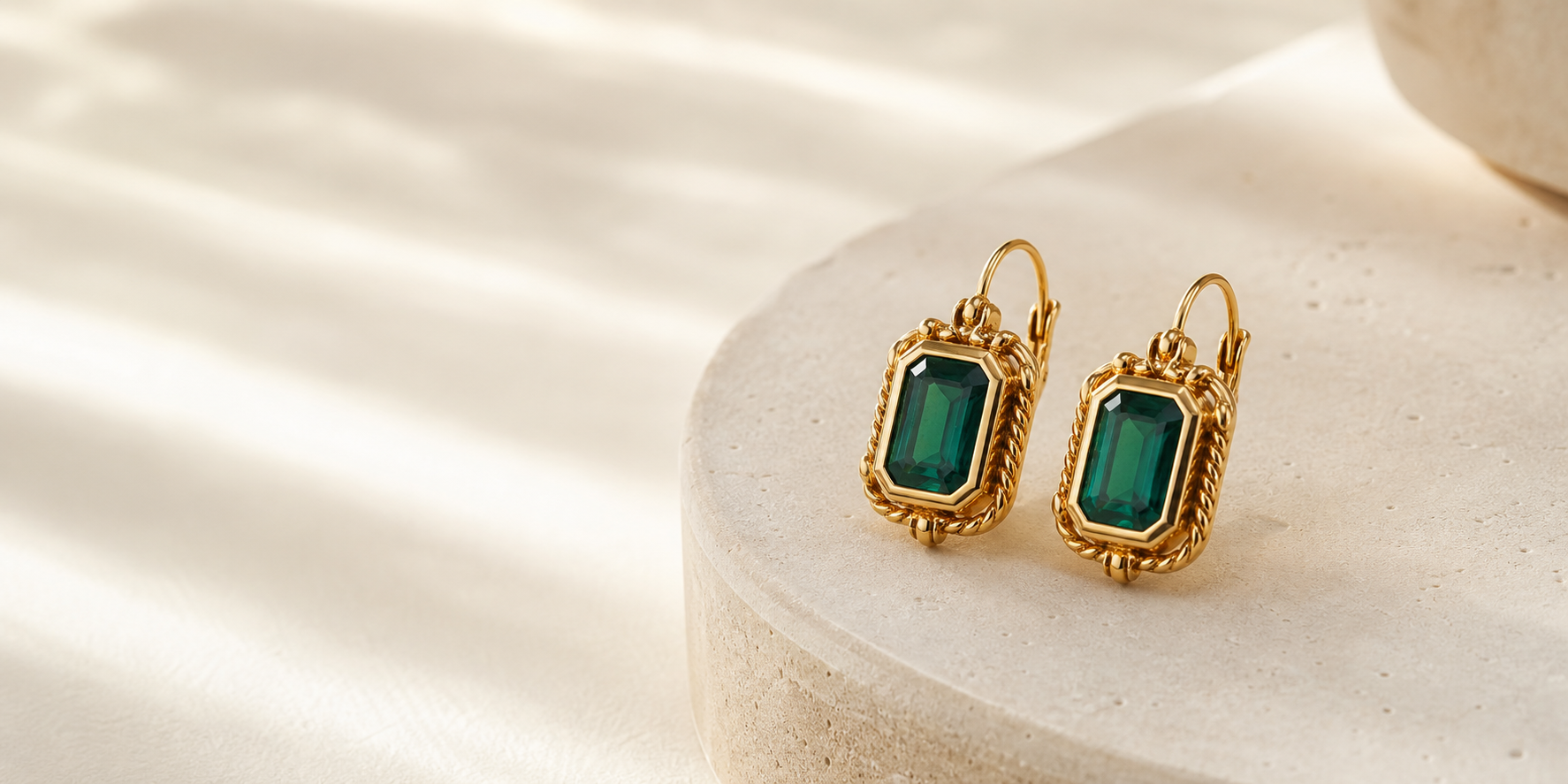 Aros dorados con piedras verdes sobre pedestal blanco